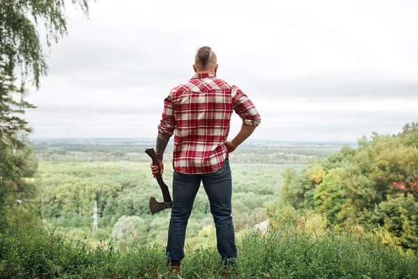 Rear view of lumberjack in forest holding an axe on his shoulder — Stock Photo, Image