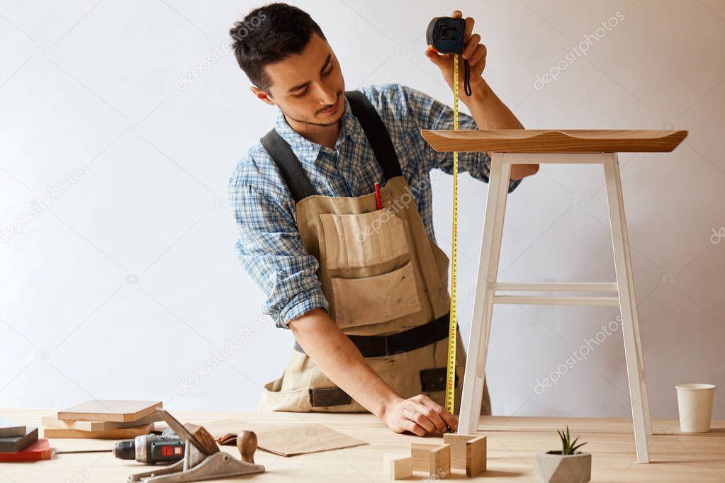 Young man measuring home furniture with measure tape. Repair concept.