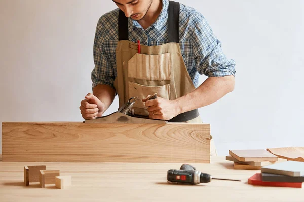 Timmerman werken met hout met behulp van vliegtuig tegen witte muur in studio. — Stockfoto