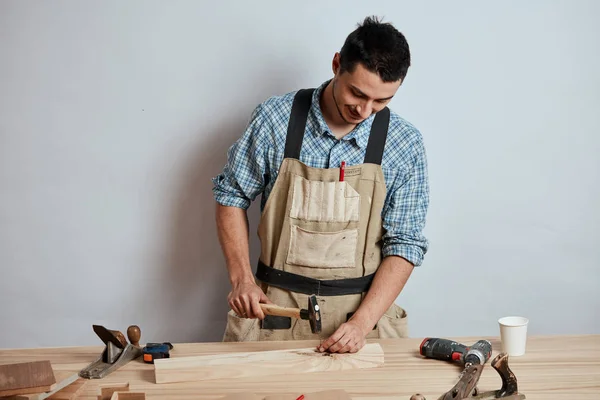 El carpintero clavando un clavo a la plancha de madera, haciendo un mueble . — Foto de Stock