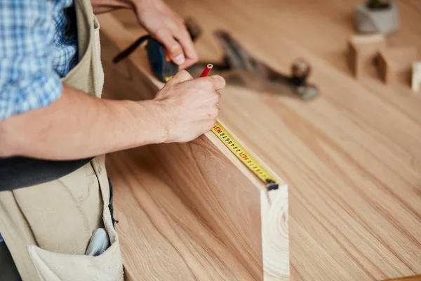 Hand van een timmerman die een houten plank meet — Stockfoto