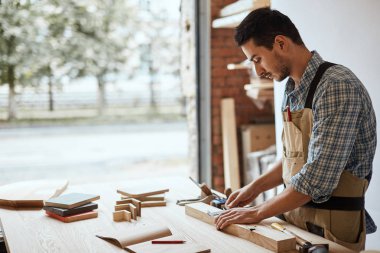 Bir marangozun eli ahşap bir tahtanın ölçüsünü alıyor.