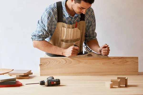 Timmerman werken met hout met behulp van vliegtuig tegen witte muur in studio. — Stockfoto