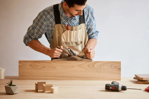 Carpenter working with wood using plane against white wall in studio. — Stock Photo, Image
