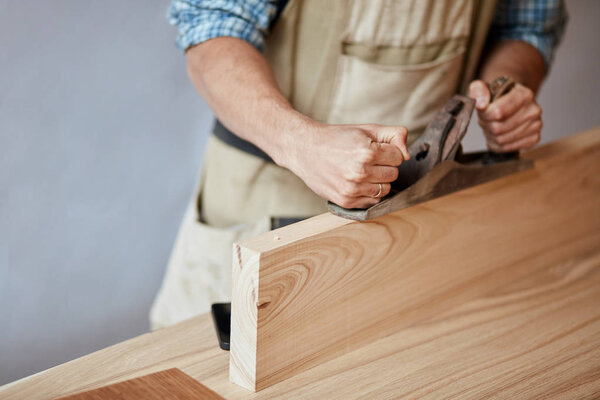 carpenter working with wood using plane against white wall in studio.