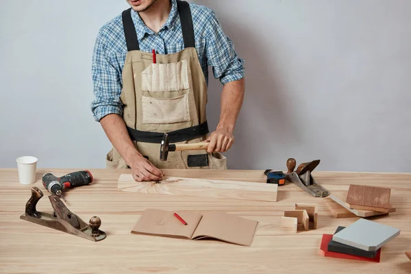 El carpintero clavando un clavo a la plancha de madera, haciendo un mueble . — Foto de Stock