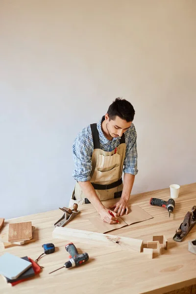 Hombre carpintero haciendo borrador plan usando lápiz sobre la mesa con herramientas — Foto de Stock