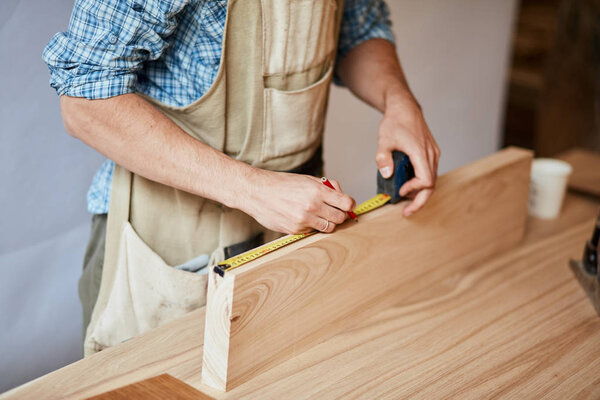 hand of a carpenter taking measurement of a wooden plank