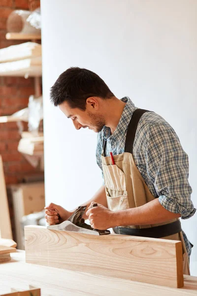 Carpenter working with wood using plane against white wall in studio. — Stock Photo, Image