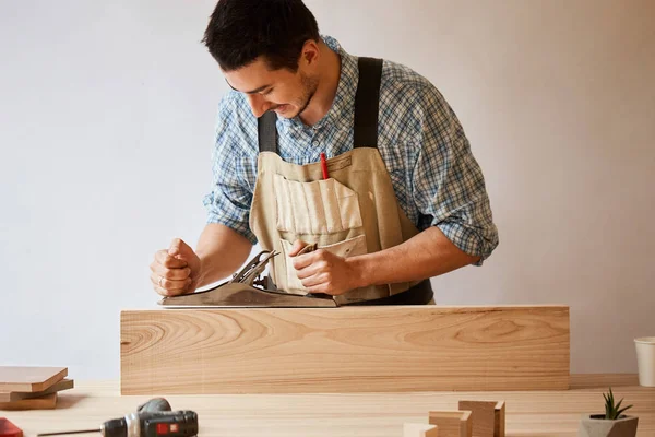 Carpintero trabajando con madera usando plano contra pared blanca en estudio. — Foto de Stock