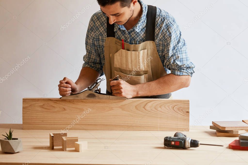 carpenter working with wood using plane against white wall in studio.