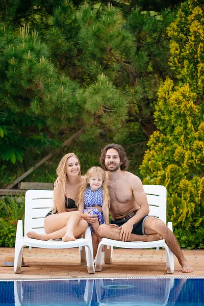 Bebê e pais relaxando na espreguiçadeira perto da piscina no resort. Meninas da moda, casal, família no resort — Fotografia de Stock