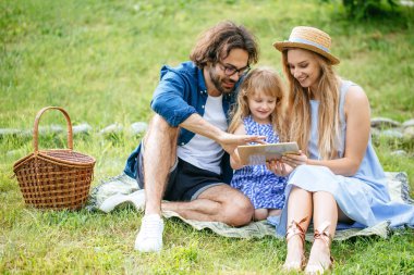Kırsal kesimde piknik yaparken dijital tablet kullanan aile