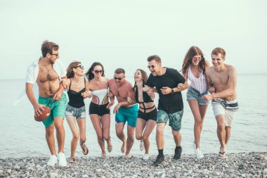 Bir grup arkadaş sahilde yürüyor, eğleniyor, kadınlar erkekleri sırtında taşıyor, komik bir tatil.