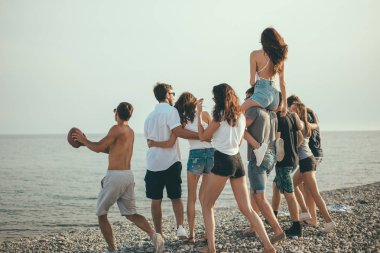 Mutlu erkekler ve kadınlar plajda yürüyüş yapar arkadaşlarıyla plaj tatilinin tadını çıkarırlar.