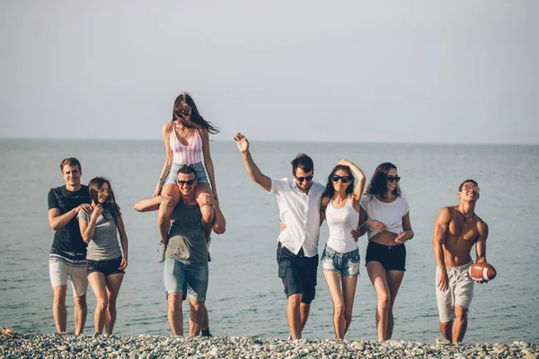 Grupo de amigos caminando en la playa, divertirse, las mujeres a cuestas en los hombres, vacaciones divertidas —  Fotos de Stock