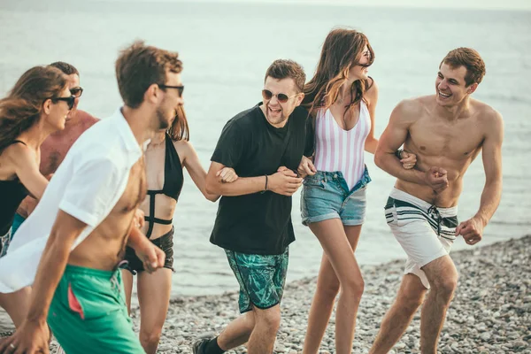 Grupo de amigos caminando en la playa, divertirse, las mujeres a cuestas en los hombres, vacaciones divertidas — Foto de Stock