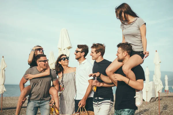 Bir grup arkadaş sahilde yürüyor, eğleniyor, kadınlar erkekleri sırtında taşıyor, komik bir tatil.