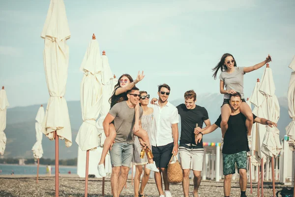 Grupo de amigos caminando en la playa, divertirse, las mujeres a cuestas en los hombres, vacaciones divertidas — Foto de Stock