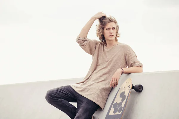 Male looking side wearing t-shirt holding wooden longboard against concrete wall — Stock Photo, Image