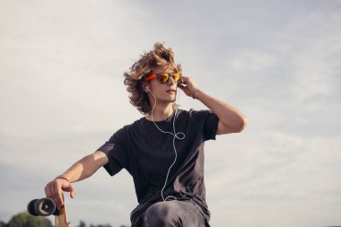 hipster adam beton duvara yakın onun telefon ve kulaklık kullanarak longboard ile ayakta