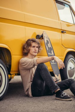 Hippi adam yolculuk sırasında sarı arabasının yanında oturuyor.