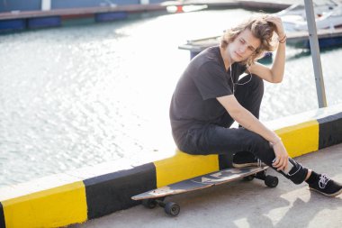 telefonunu kullanarak longboard üzerinde oturan hipster adam