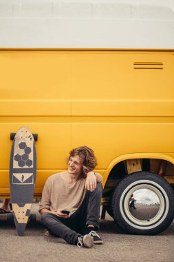 telefonunu kullanarak longboard üzerinde oturan hipster adam