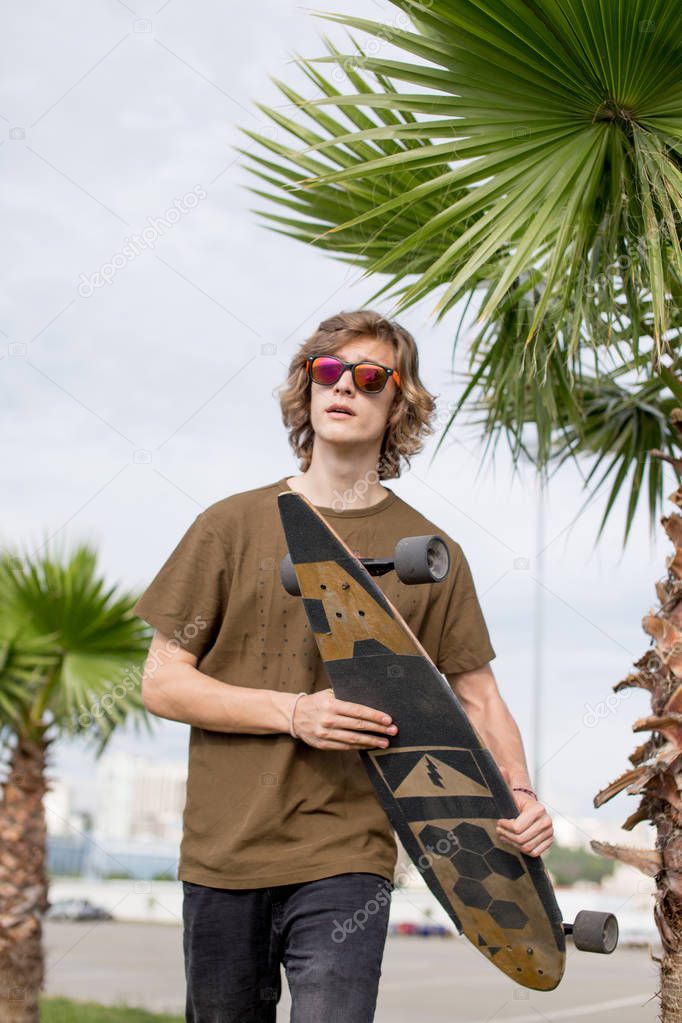 Stylish man stands on street and hold long board in hands