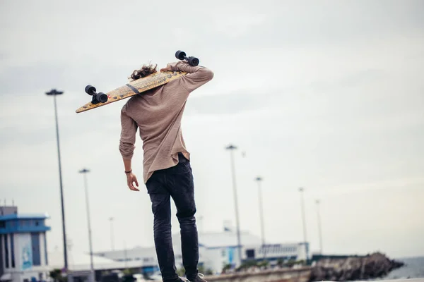 Man permanent met skateboard op zijn schouder en opzij op zoek — Stockfoto