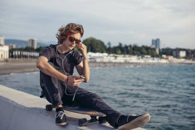 telefonunu kullanarak longboard üzerinde oturan hipster adam