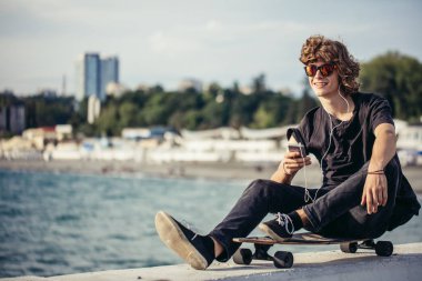 telefonunu kullanarak longboard üzerinde oturan hipster adam