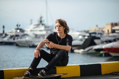 telefonunu kullanarak longboard üzerinde oturan hipster adam