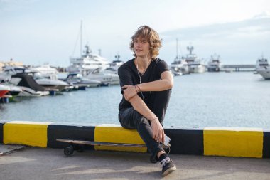 telefonunu kullanarak longboard üzerinde oturan hipster adam