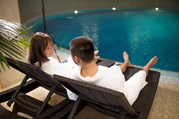 Dois casais amorosos sentados em roupões de banho junto à piscina — Fotografia de Stock