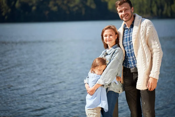 Щаслива сім'я дивиться на камеру, позує на пірсі на тихому озері — стокове фото