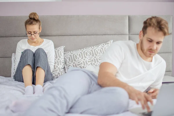 Boos vrouw in glazen lezen van een boek terwijl haar echtgenoot met behulp van laptop — Stockfoto