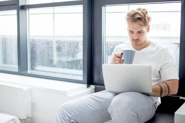 Goed uitziende man met laptop en drinken koffie thuis — Stockfoto
