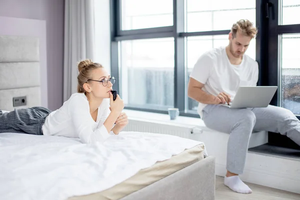 Ernstige blonde vrouw staren op Tv, terwijl haar vriendje is het verzenden van e-mail — Stockfoto