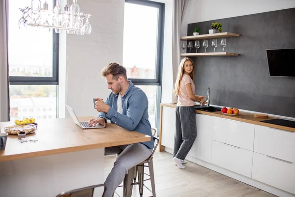 Wunderschöne Frau putzt die Küche, während ihr Mann im Netz surft — Stockfoto