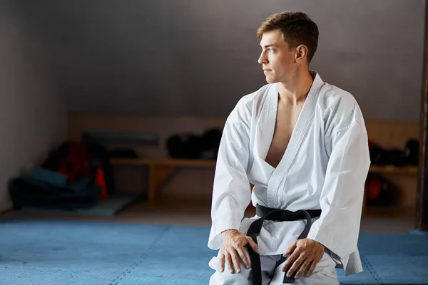Karate man in kimono zit op knieën op de vloer in de sportzaal martial arts — Stockfoto