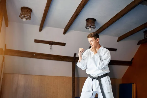 Hombre en kimono blanco con cinturón negro entrenamiento karate en gimnasio — Foto de Stock