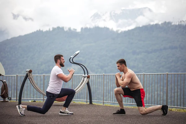Zijaanzicht van twee Kaukasische sporters doen lungesin bergen. — Stockfoto
