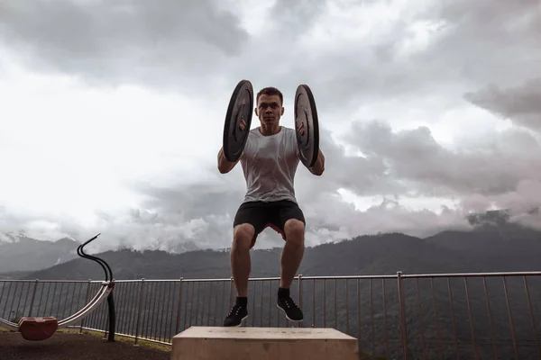 Forte atleta maschio che fa salti box con due piastre all'aperto in cima alla montagna. — Foto Stock