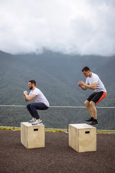 Kaukasische mannelijke atletische vrienden doen vak springen buiten op de top van de berg. — Stockfoto