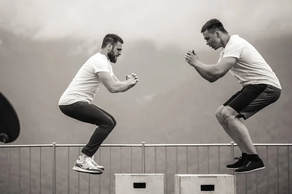 Dos amigos atléticos masculinos haciendo salto de caja al aire libre en la cima de la montaña. — Foto de Stock