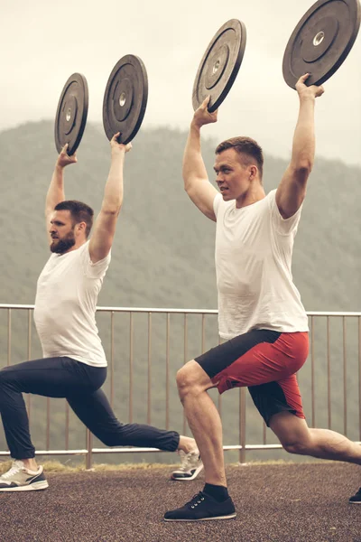 Dos atletas con disco de barra haciendo embestidas en el entrenamiento al aire libre — Foto de Stock