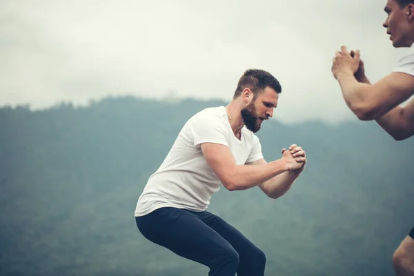 Dos amigos atléticos masculinos haciendo salto de caja al aire libre en la cima de la montaña. — Foto de Stock