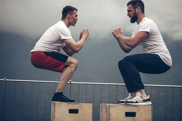 Dos amigos atléticos masculinos haciendo ejercicio de salto de caja al aire libre — Foto de Stock