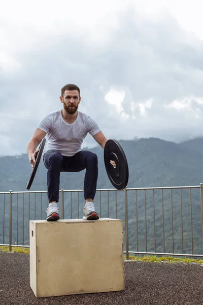 Stark manlig idrottsman gör box hopp med två plattor utomhus på toppen av berget. — Stockfoto
